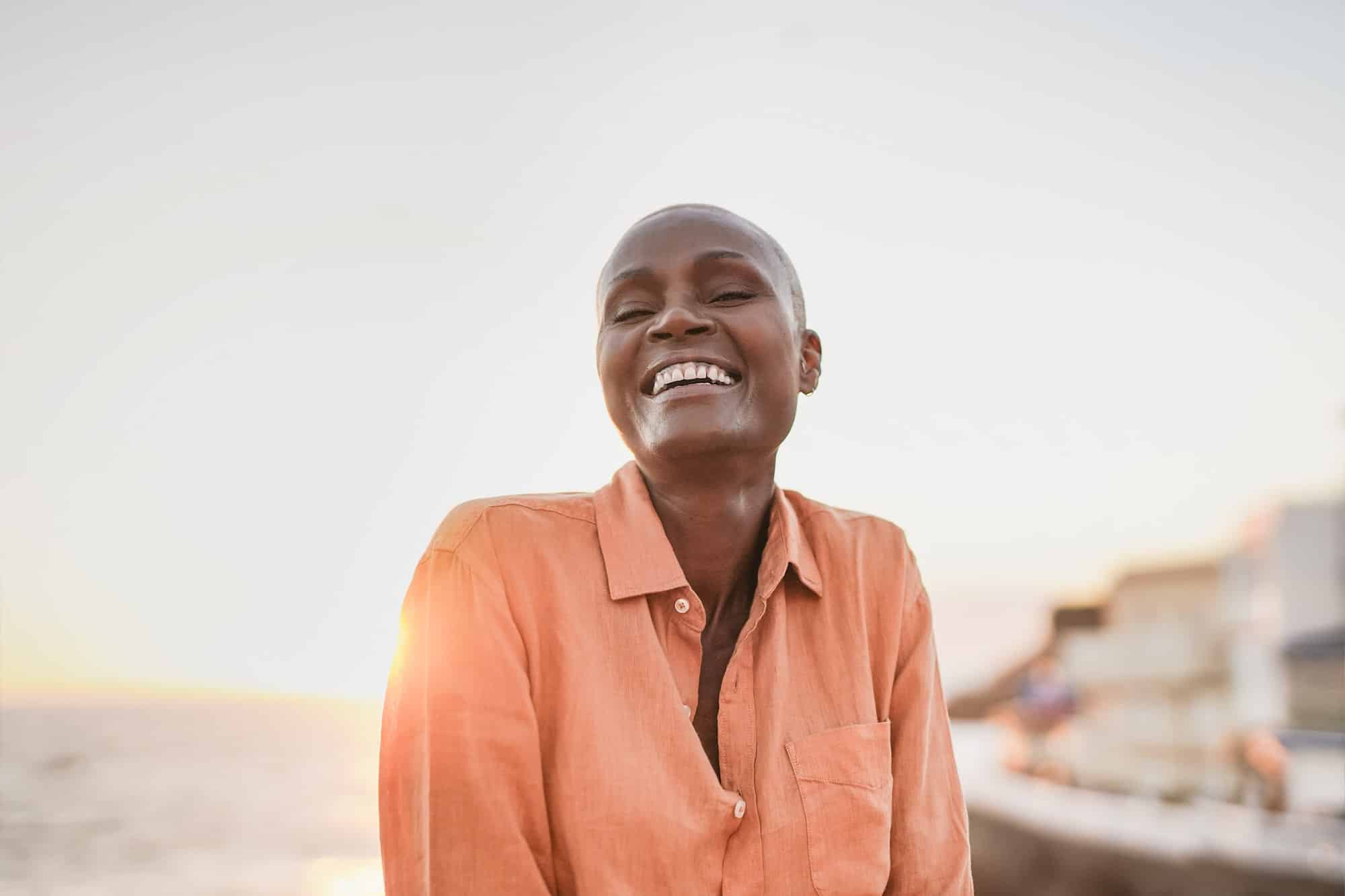 Mature afriacan woman smiling on camera outdoor with ocean and sunset in background
